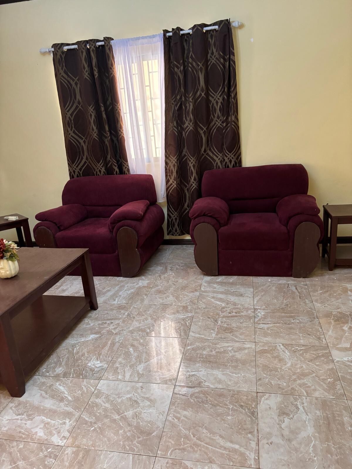 A living room with two red sofas, a wooden coffee table, and a window with patterned curtains.