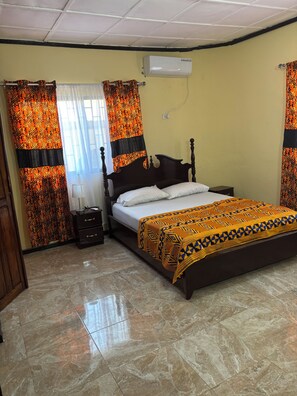 Un dormitorio con cama, cortinas, aire acondicionado y mesita de noche.