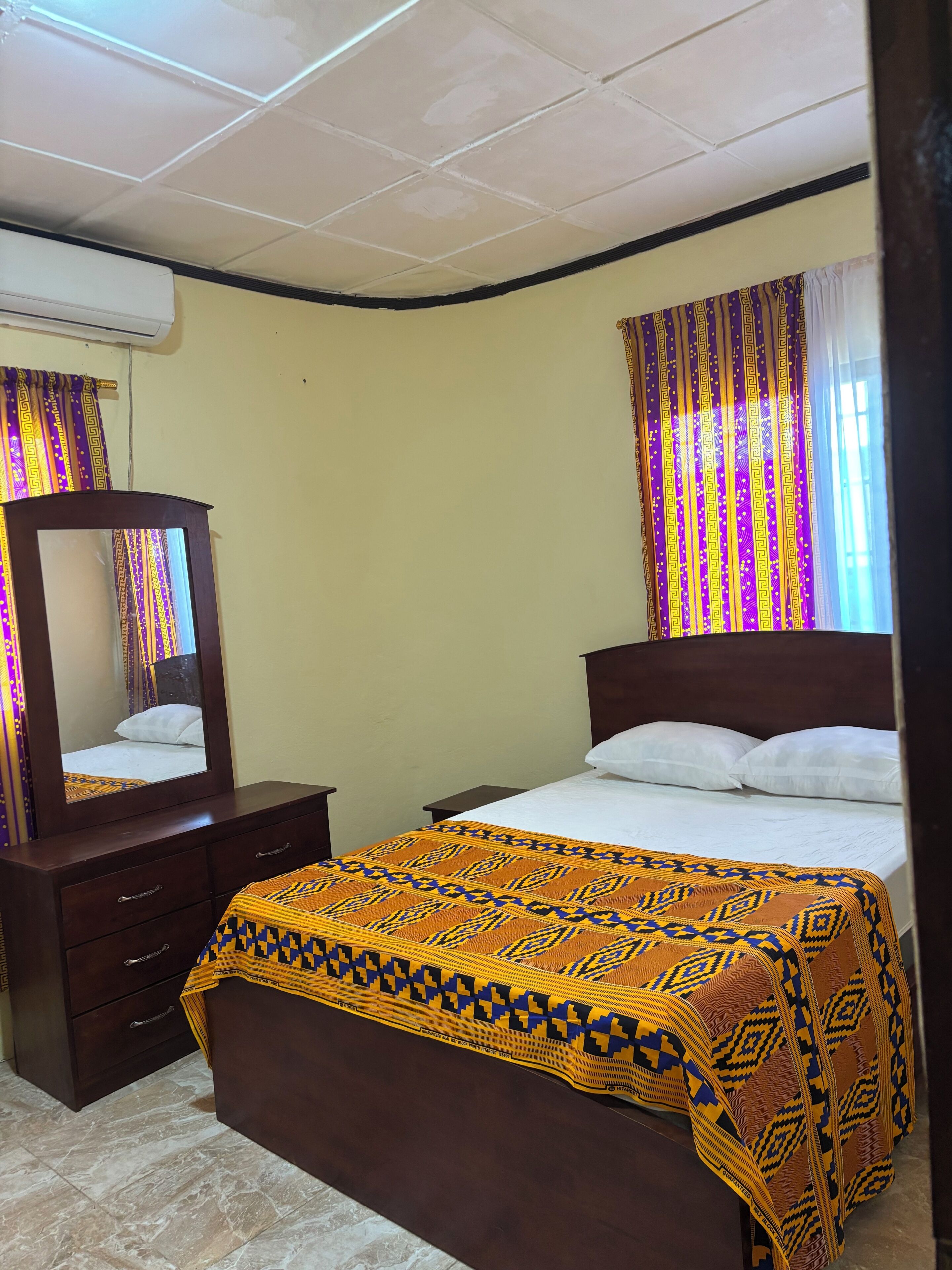 Quarto com cama, cômoda, espelho, cortinas e janela.