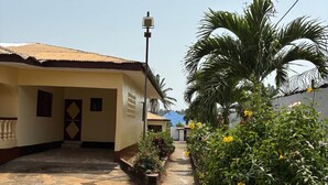 A narrow pathway leading to a building with a tiled roof and a small garden area with plants and flowers.