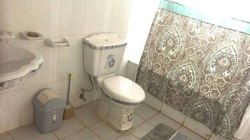 Baño con inodoro, lavamanos, cubo de basura y escoba.