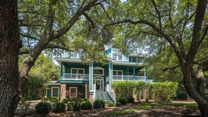 A two-story house with a front porch, surrounded by trees and a well-maintained lawn. - Las Brisas: New Rental, Large Private Pool, Hot Tub (Corolla)