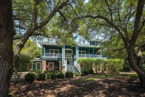 A two-story house with a front porch, surrounded by trees and a well-maintained lawn. - Las Brisas: New Rental, Large Private Pool, Hot Tub (Corolla)