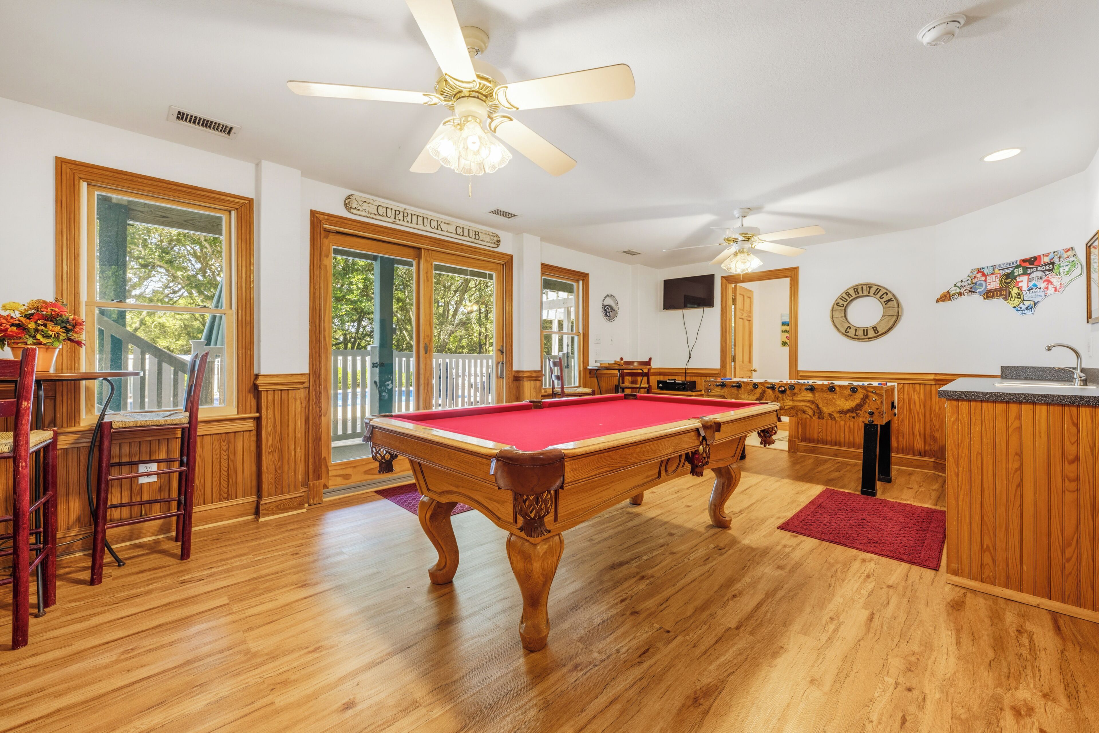 A pool table in a room with wooden floors, a ceiling fan, and a sign reading 'Curryduck Club'.