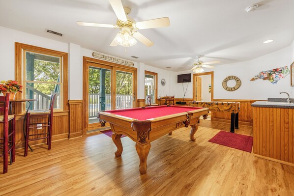 A pool table in a room with wooden floors, a ceiling fan, and a sign reading 'Curryduck Club'.