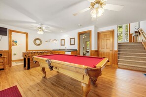 A pool table in a room with wooden floors, a ceiling fan, and a staircase. - Las Brisas: New Rental, Large Private Pool, Hot Tub (Corolla)