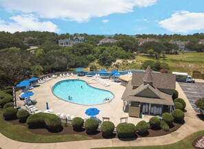 A swimming pool with lounge chairs and umbrellas, surrounded by well-maintained bushes and a building with a pitched roof.