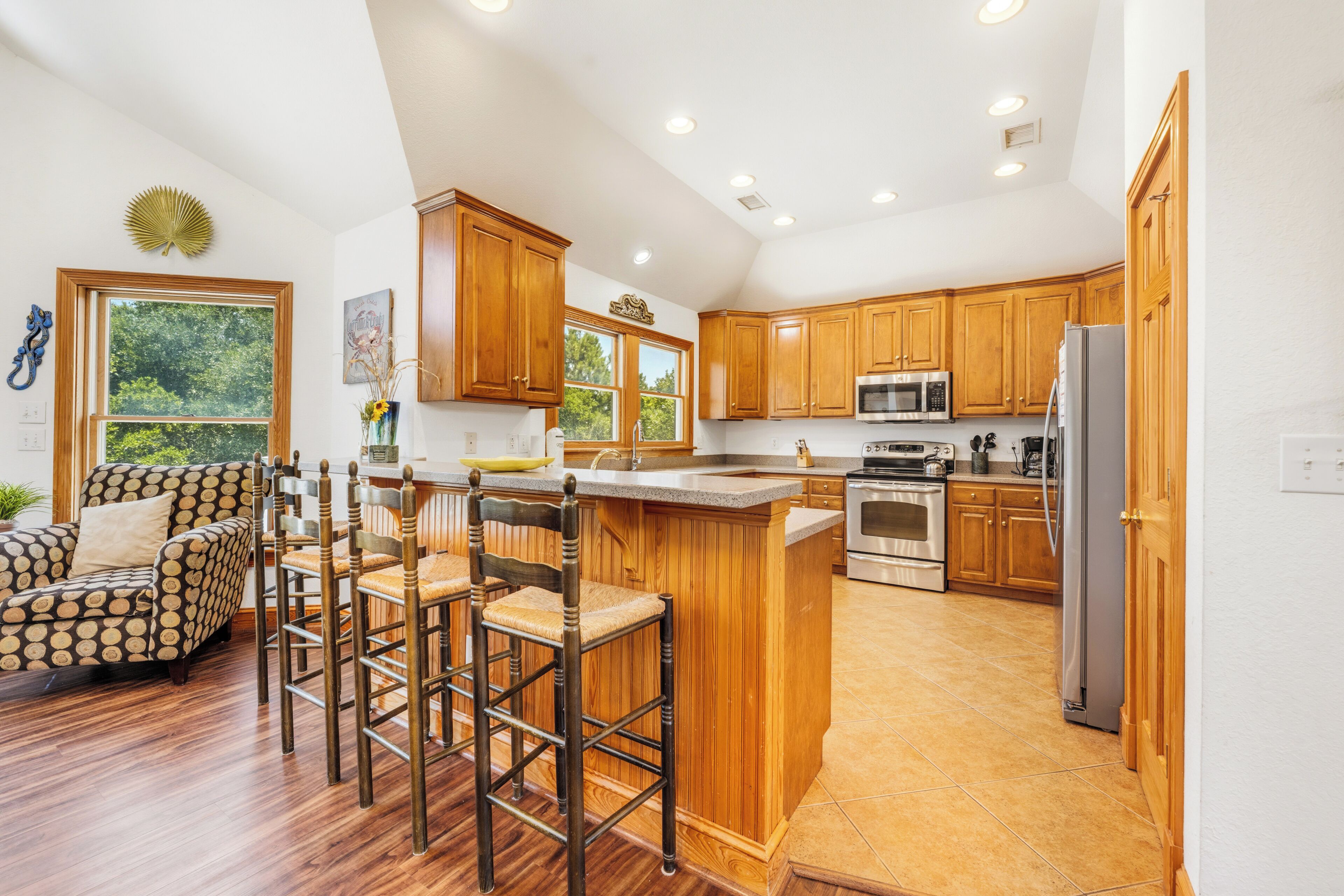 A kitchen with wooden cabinets, a large island, and a dining area with patterned chairs.