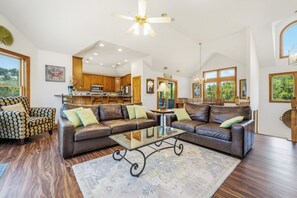 A spacious living room with a large brown leather sofa set, a glass coffee table, and a wooden floor.