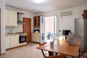 Eine kompakte Küche mit Herd, Backofen und Mikrowelle, ein Essbereich mit Tisch und Stühlen sowie eine Glastür zum Balkon.