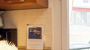 Ett kök med en mikrovågsugn, en tryckt annons för ”Alghero Holiday House” och ett fönster med utsikt över omgivningen.