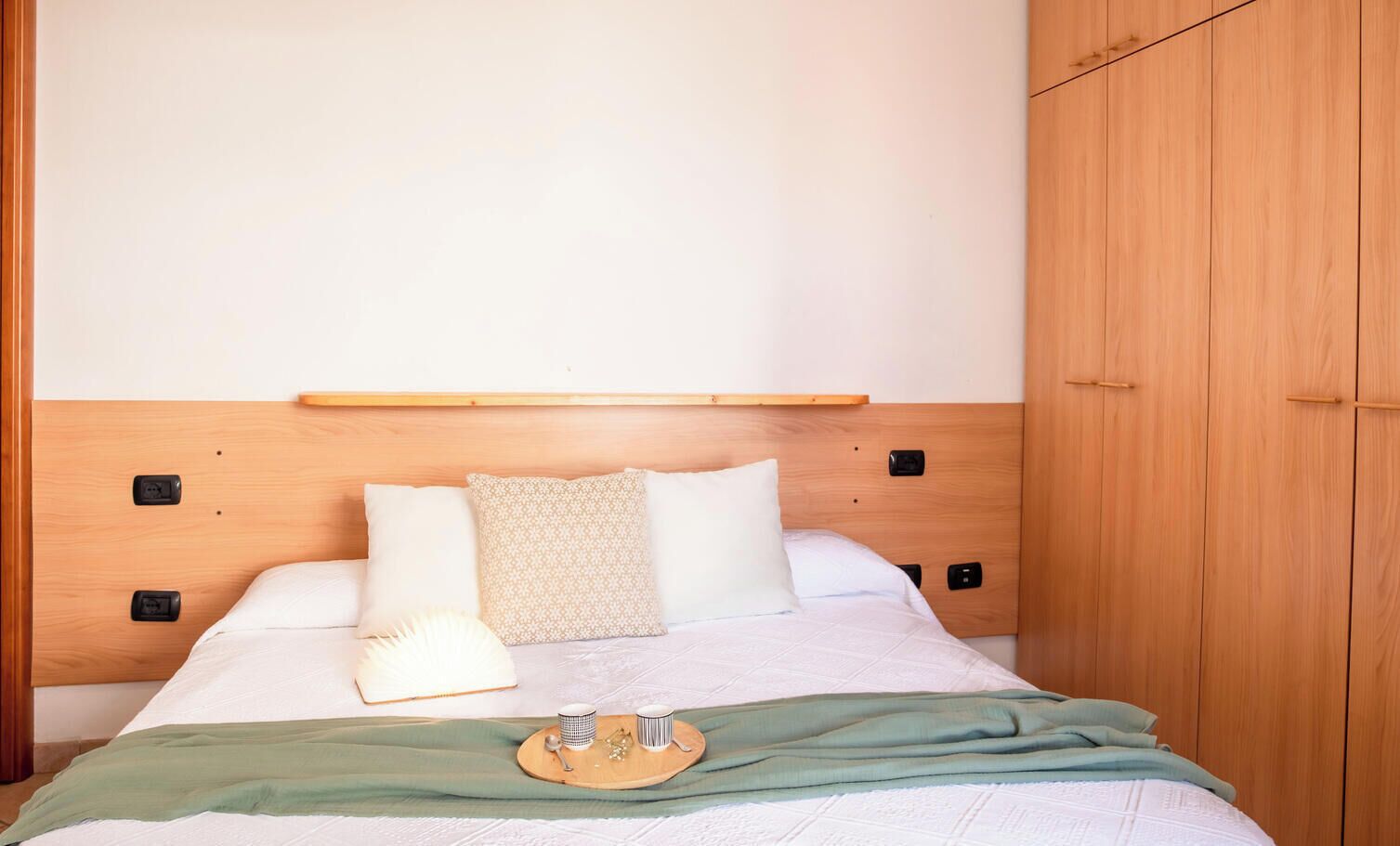 A neatly made bed with a wooden headboard, a bedside table with a tray, and a wardrobe.