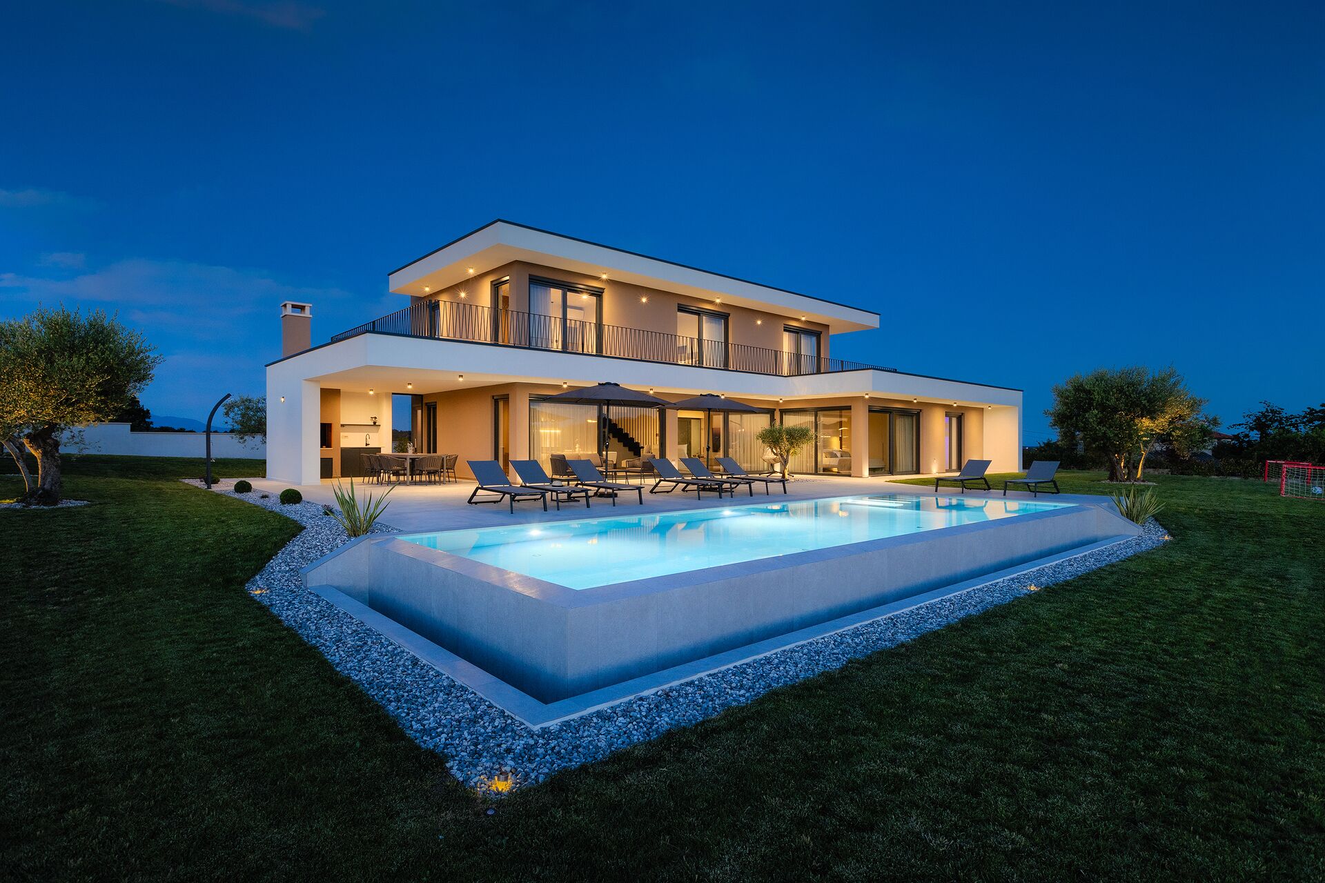 Una casa moderna de dos pisos con piscina, mobiliario exterior y césped cuidado.