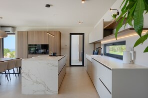 A modern kitchen with a marble island, wooden cabinets, and a view of the outdoors. - Villa Horizonte Verde (Istria - Motovun) (Motovun)