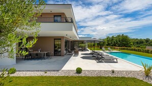 Uma casa moderna de dois andares com piscina, área de estar externa e um jardim bem cuidado.