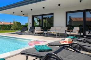 Ein Poolbereich mit Liegestühlen, einem Tisch und einer überdachten Sitzecke.