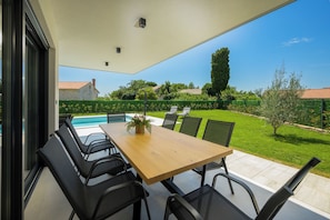 Eine Terrasse mit Holztisch und -stühlen, einem Pool und Blick auf einen Garten und Häuser.