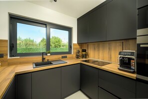 A modern kitchen with a large window, dark cabinetry, and a coffee machine. - Villa Luna Kanfanar (Istria - Kanfanar) (Kanfanar)