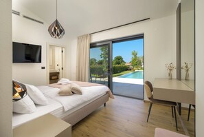 A modern bedroom with a bed, a TV, a desk, and a sliding glass door leading to a pool. - Villa Lunique (Istria - Rovinj) (Rovinj)