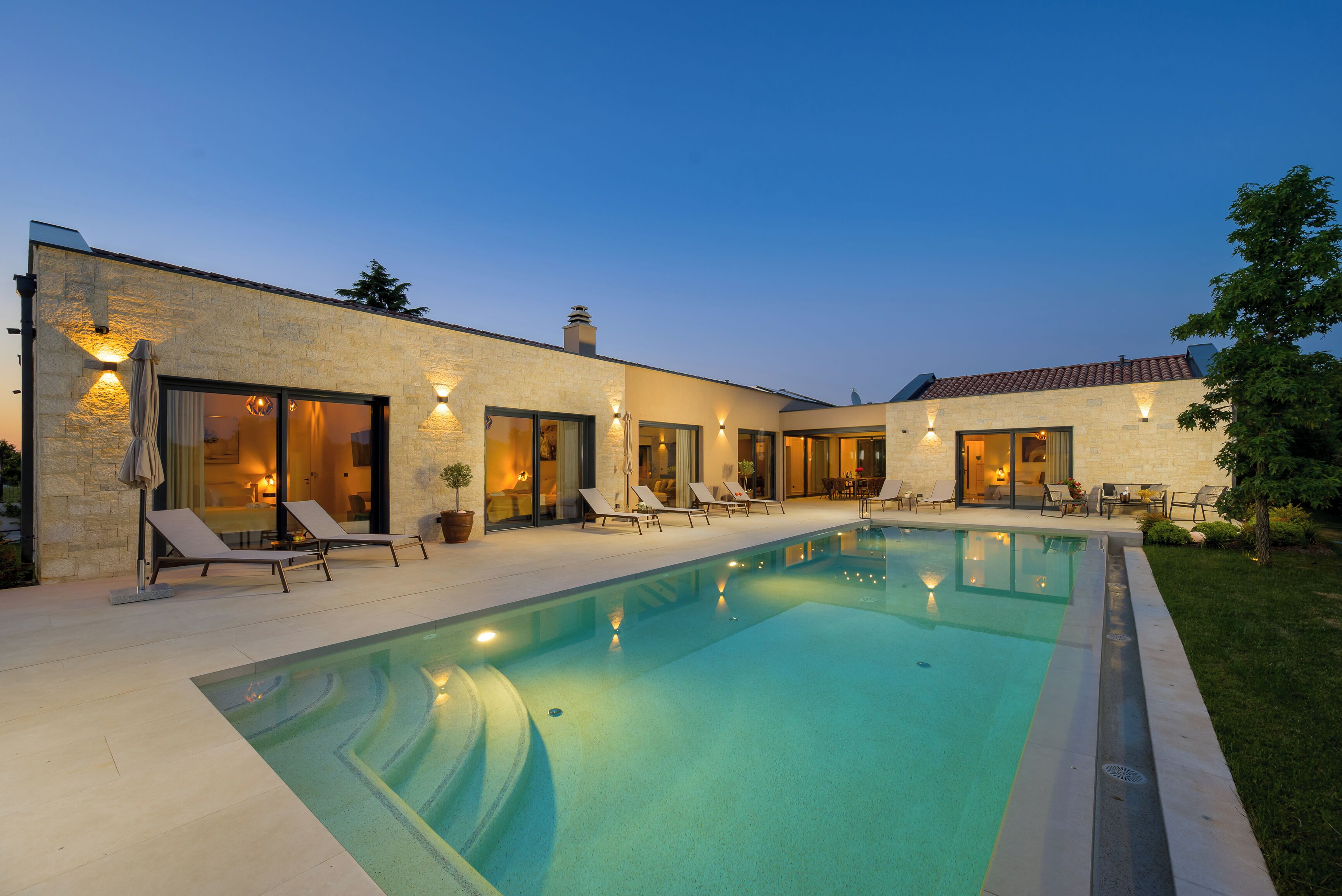 Une maison moderne dotée d’une piscine, de chaises longues et d’un patio bien éclairé.