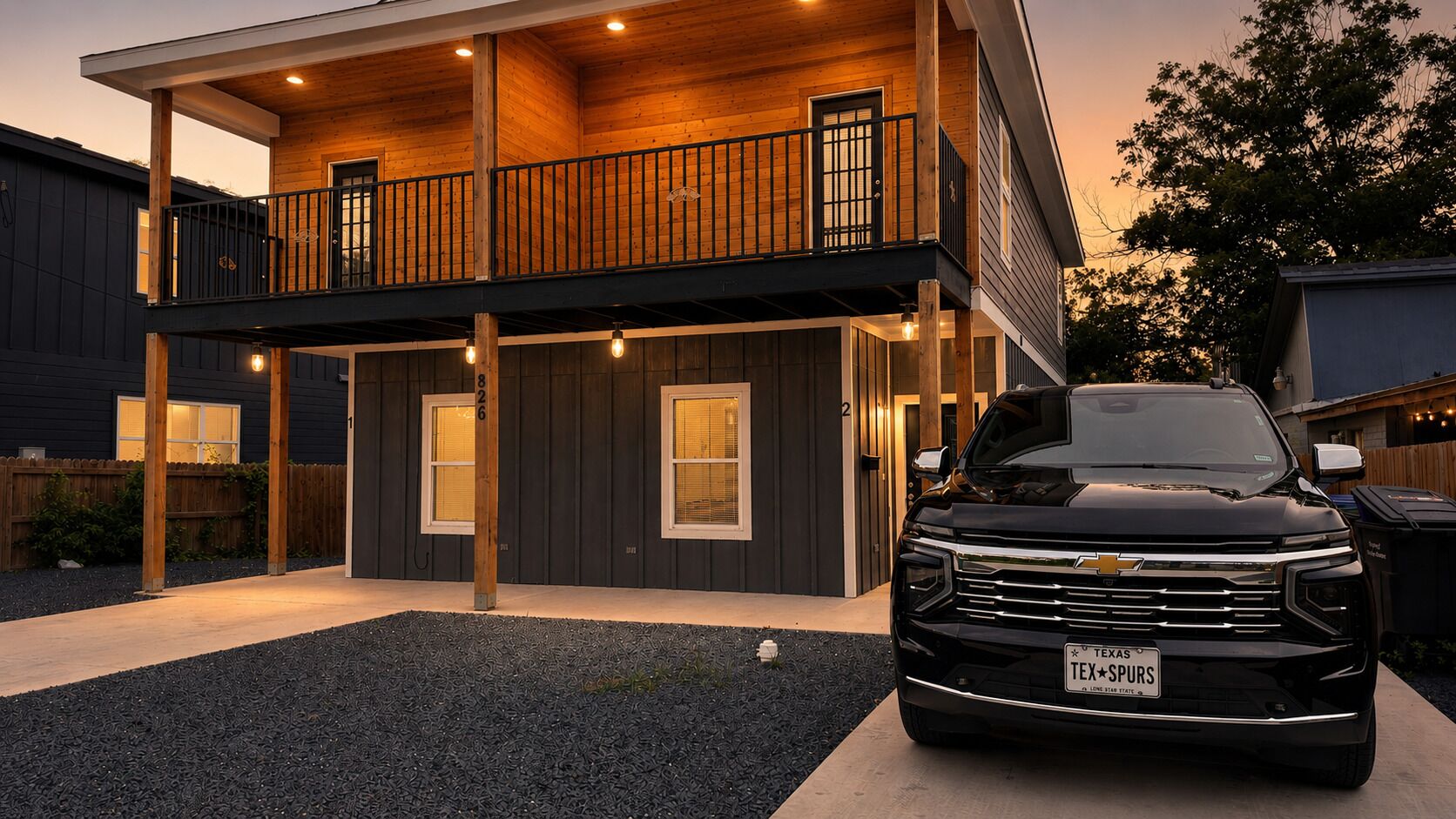 A modern two-story house with a balcony, a driveway, and a black pickup truck parked in front.