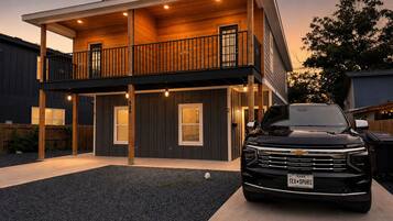 A modern two-story house with a balcony, a driveway, and a black pickup truck parked in front.