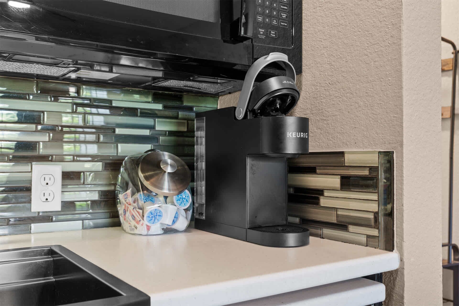 A kitchen with a coffee maker, a glass jar with a lid, and a power outlet.