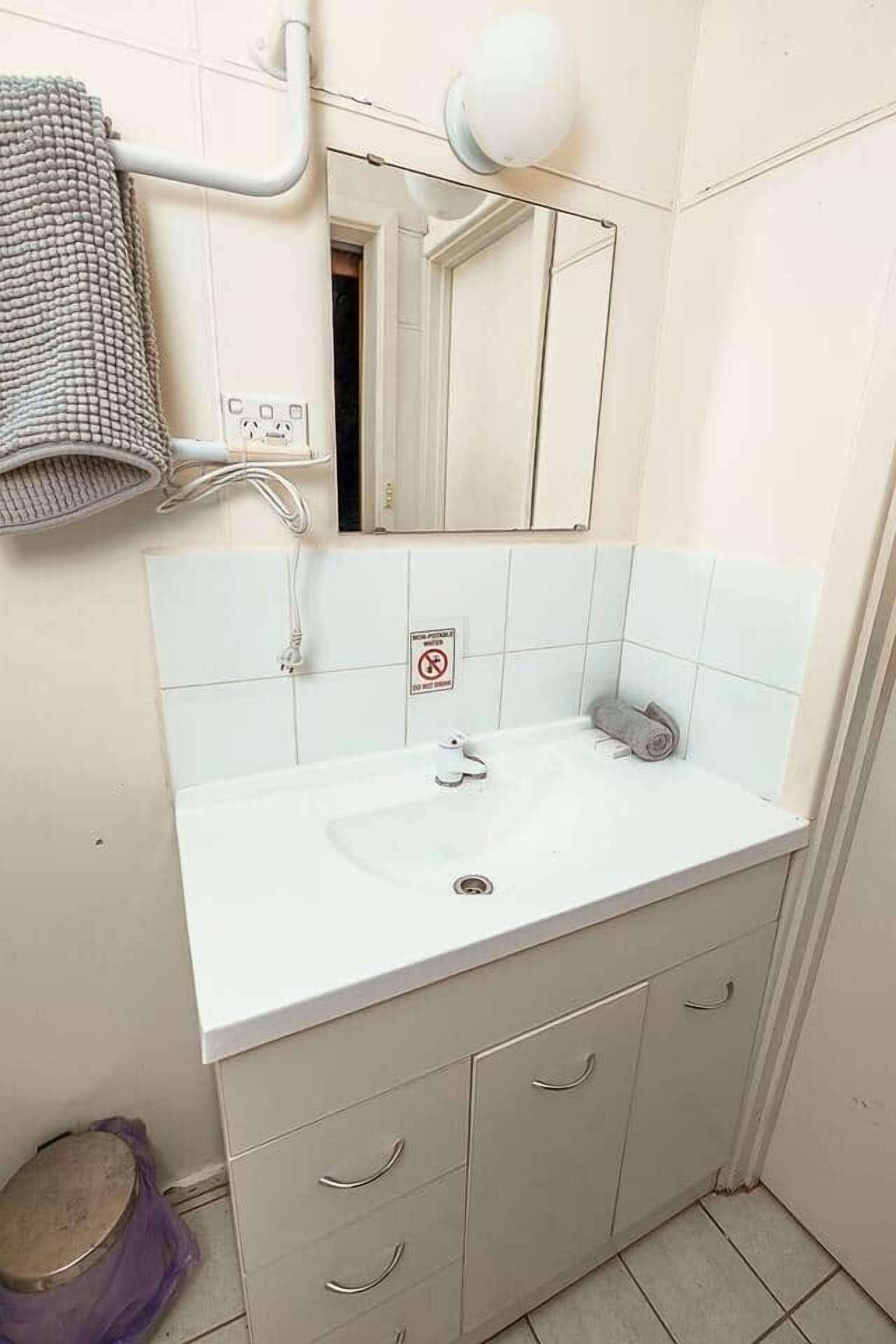 Un bany amb un lavabo blanc, un mirall i un penjallot de tovalloles.