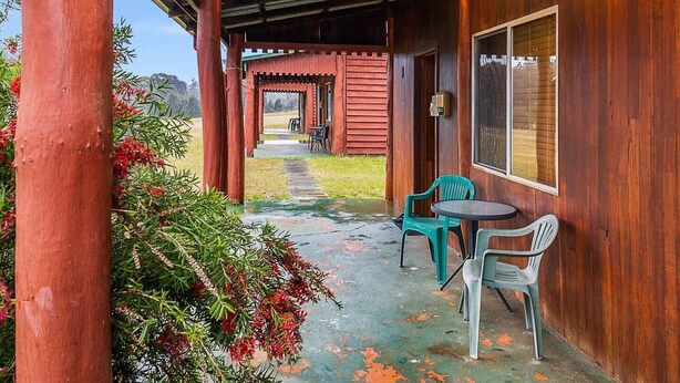 A covered porch with wooden pillars, a pathway leading to a building, and two plastic chairs.