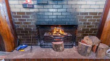 A fireplace with a fire, a brick wall, and a wooden bench.