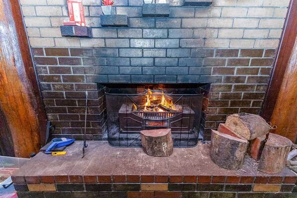 A fireplace with a fire, a brick wall, and a wooden bench.