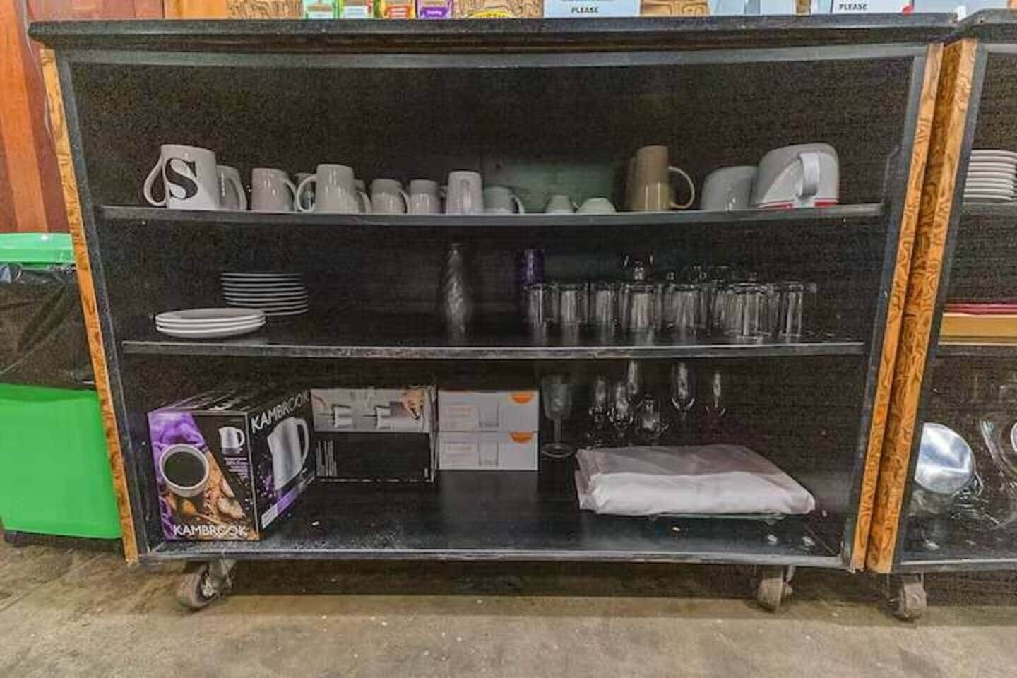 A shelf with various items including cups, plates, and a box labeled 'KAMBROOK.'