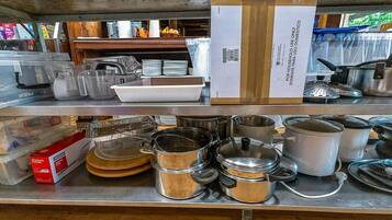 Een keuken met roestvrijstalen pannen en braadpannen, een doos wegwerpmessen, en een stapel witte borden.