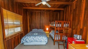 Una habitación de madera con una cama litera, una cama individual, un escritorio y un ventilador de techo.