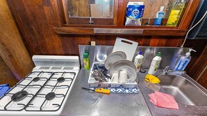 Una cocina con estufa a gas, pileta de acero inoxidable y diversos productos de limpieza.
