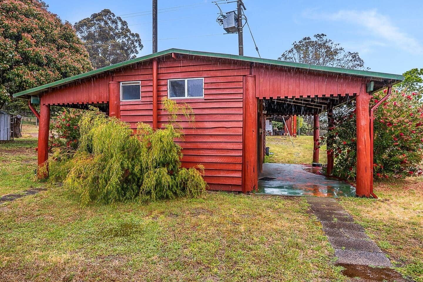 A red wooden structure with a covered porch, surrounded by grass and shrubs.