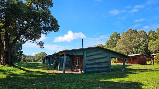 A rustic cabin with a porch, surrounded by lush greenery and trees.