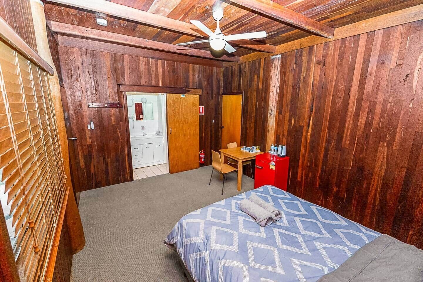 Ein Zimmer mit einem Bett, einem Schreibtisch, einem Stuhl, einem Spiegel und einem Deckenventilator.