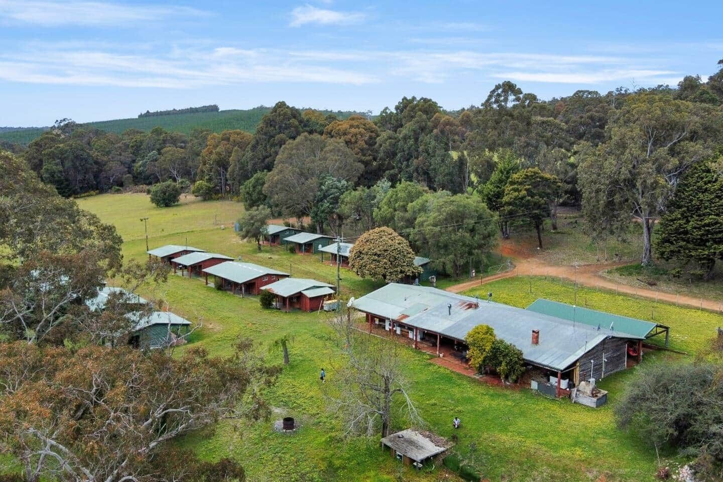 A rural property with multiple cabins, a large open field, and dense forest in the background.