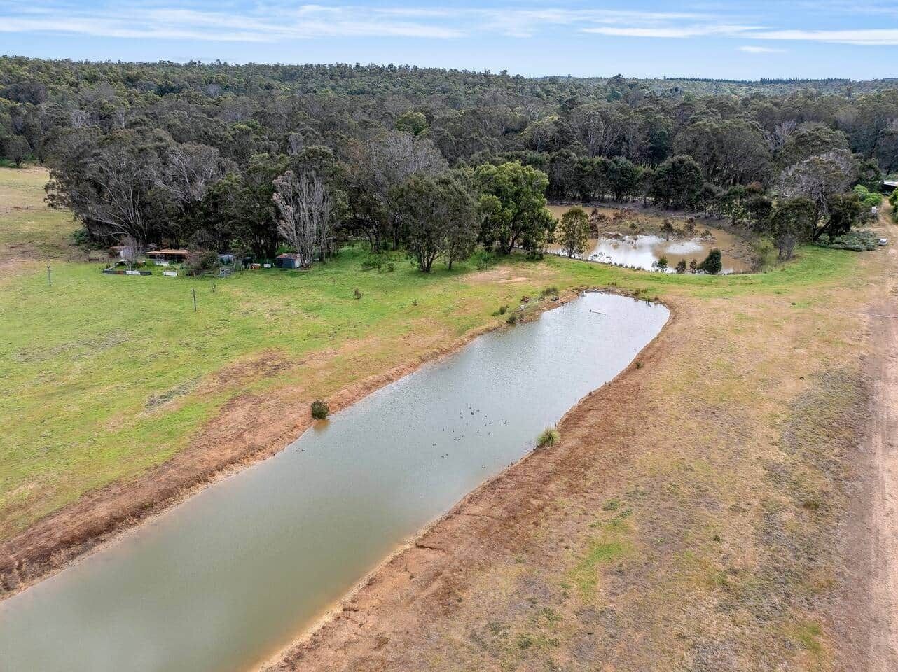 A river meandering through a rural landscape with trees and a few buildings in the distance.
