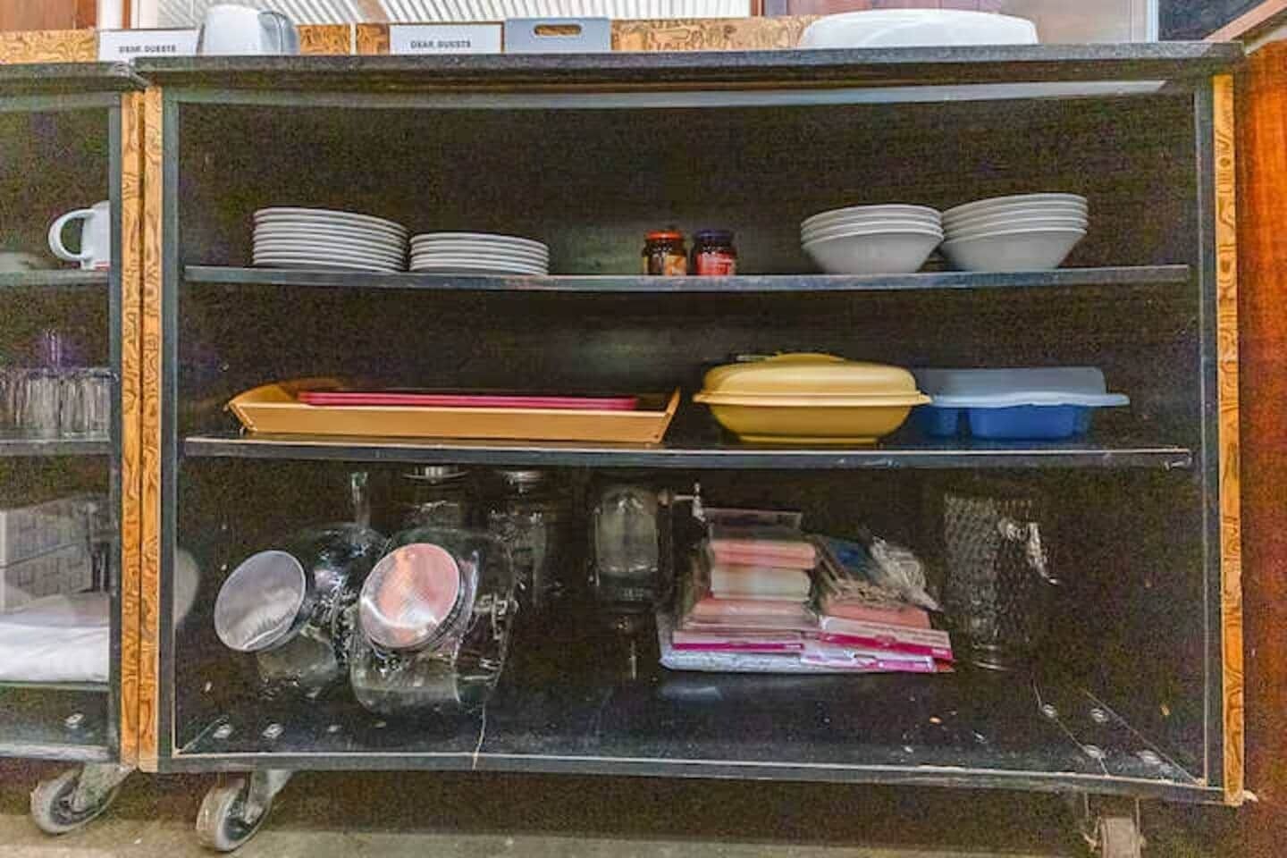 A kitchen cart with shelves holding plates, bowls, jars, and kitchen utensils.