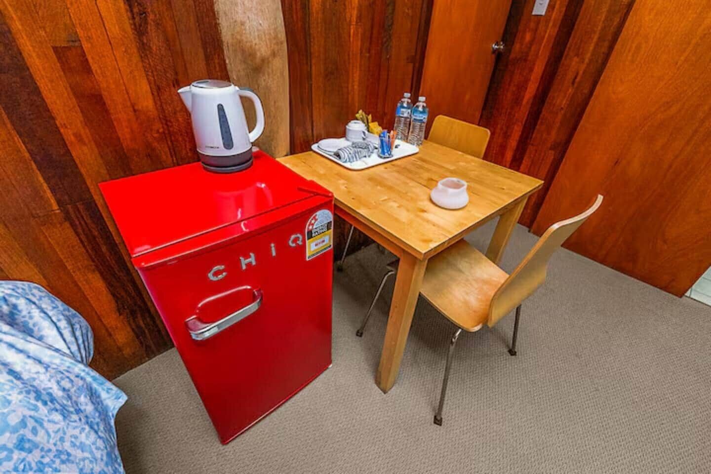 Ein kleines Zimmer mit roter Küchenzeile, einem Holztisch und einem einzelnen Stuhl.
