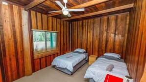 Una habitación con paneles de madera, dos camas, un ventilador de techo y una ventana con persianas.