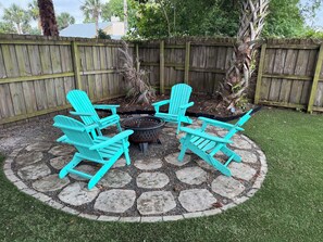 Eine Terrasse mit vier türkisfarbenen Adirondack-Stühlen, die um eine Feuerstelle angeordnet sind, auf einem Steinrund.