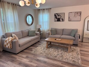 Ein Wohnzimmer mit zwei Sofas, einem Couchtisch, einer Lampe und einem Teppich.