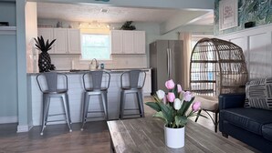 A modern kitchen with white cabinets, a stainless steel refrigerator, and a dining area with bar stools. - AZURE TIDES BEACH HOUSE (Panama City Beach)