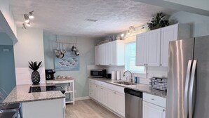 A modern kitchen with white cabinets, a stainless steel refrigerator, a microwave, and a coffee maker. - AZURE TIDES BEACH HOUSE (Panama City Beach)