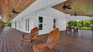 A covered wooden deck with Adirondack chairs, ceiling fans, and a view of greenery. - Bleu Hermitage | Private 25-Acre Luxury Sanctuary (Naples)