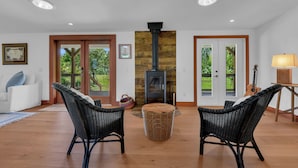 A living room with a fireplace, wicker chairs, a round ottoman, and a guitar. - Bleu Hermitage | Private 25-Acre Luxury Sanctuary (Naples)