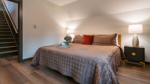A bedroom with a bed, a nightstand, a lamp, a tray with items, and a staircase. - Alpine Evergreen | Upscale A-Frame | Pet Friendly Cabin in Helen, GA (Helen)